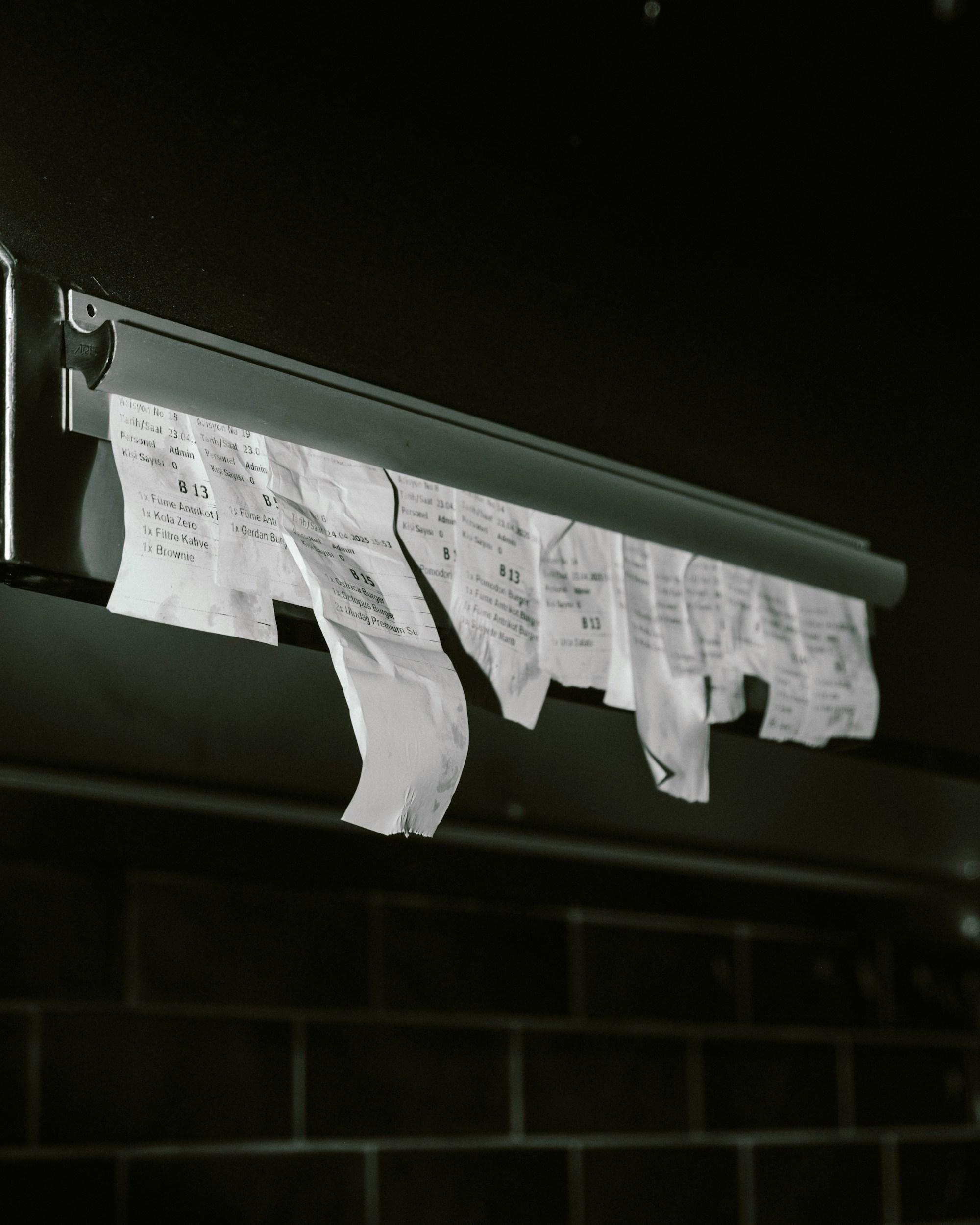 Printed kitchen order tickets hanging from a metal chit rail at the pass.