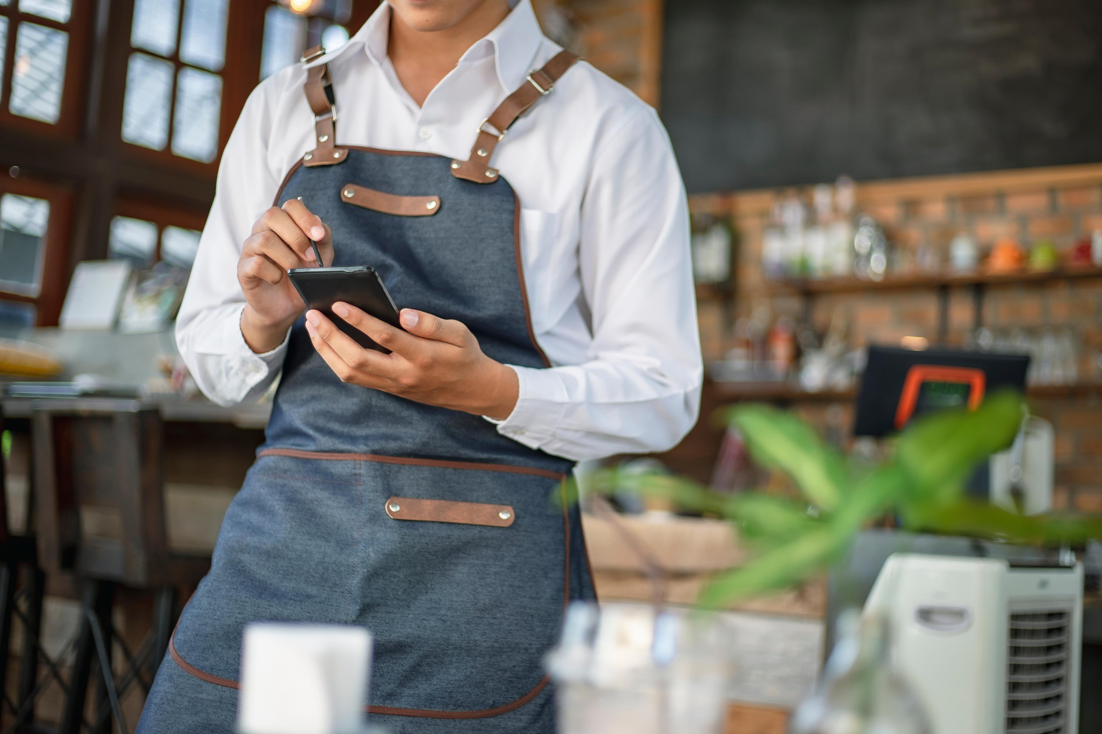 A server in an apron checking a smartphone during service.